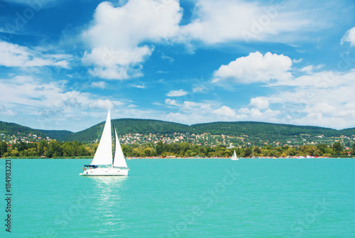 Panoramic view of lake river blue transparent water, a white sport modern luxury yacht sail boat floating and a green shore with forest, hills, villages and beach Fototapeta