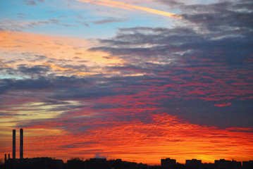 Colorful red orange dark dramatic evening sky over industrial landscape with two chimneys and a cloud of dark smoke. Copy space for text.