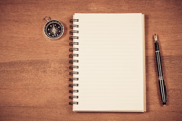 vintage compass on book note and fountain pen on wood table.