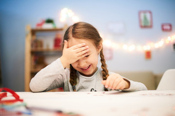 Wall Mural - Cute little girl with two braids sitting at desk in cozy bedroom and thinking over design of future Christmas card, portrait shot