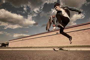 People, leisure, hobby, recreation and active lifestyle concept. Picture of flying guy in the air with longboard while doing tricks during every day practice in cityscape. Warm filter, toned image