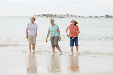 Wall Mural - group of three senior mature retired women on their 60s having fun enjoying together happy walking on the beach smiling playful