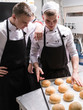 © Photodrive - Freshly baked hamburger rolls. Young cooks checking the quality of the buns looking for flaws and seeking perfection. Communication and teamwork concept