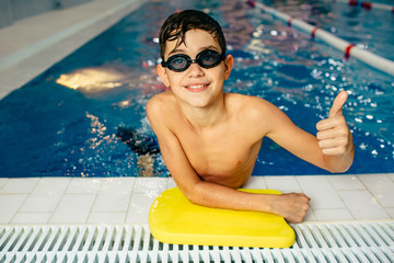 Boy wearing swim goggles, in the swimming pool showing thumbs up and looking at camera. children, swimmer.