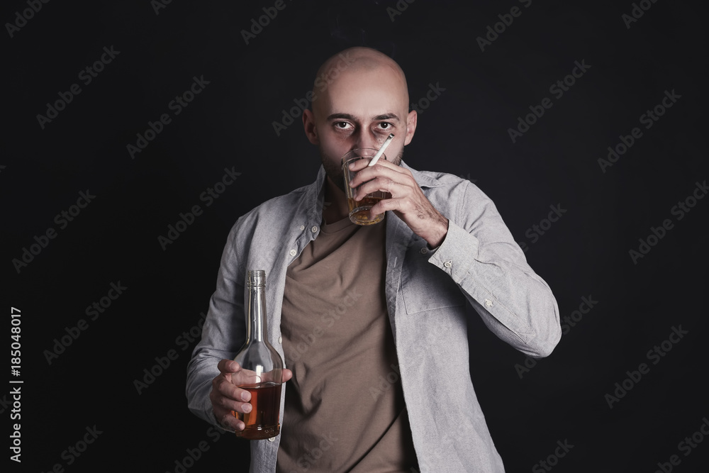 Man drinking whiskey and smoking cigarette on dark background. Alcoholism concept