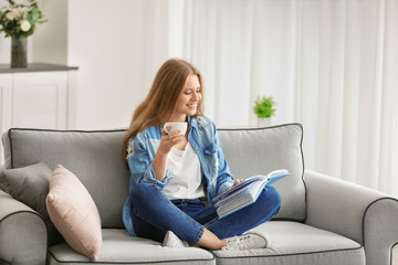 Wall Mural - Beautiful woman reading book while resting on sofa at home