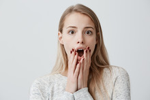Young Blonde Woman With Dark Eyes Dressed Casually, Staring With Big Eyes At Camera And Widely Opened Mouth Being In Panic Worried To Hear Bad News. Horrified Girl With Shocked Scared Look