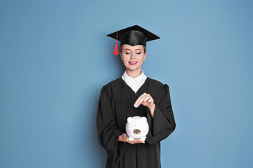 Poster - Young graduate putting coin into piggy bank on color background