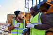© Seventyfour - Portrait of two workers, one African-American, drinking coffee and chatting next to heavy industrial truck on worksite