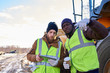 © Seventyfour - Portrait of two workers, one African-American, drinking coffee and using digital tablet standing next to heavy industrial truck on worksite, copy space