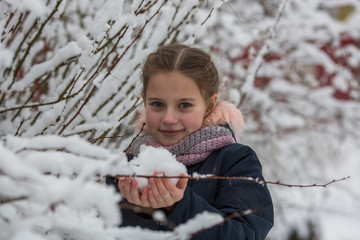 Cute little girl holds snow in hands.