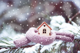 Fototapeta Mapy - Christmas Toy house is wrapped in a warm scarf, it's snowing.on a natural natural background of a real fir in the snow, toned. Concept of winter, Christmas, new year,