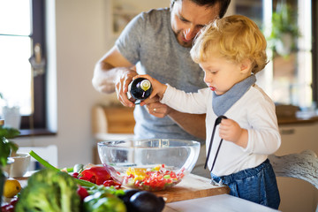 Wall Mural - Young father with a toddler boy cooking.