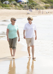 Wall Mural - two lovely senior mature retired women on their 60s having fun enjoying together happy walking on the beach smiling playful