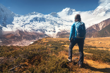 Wall Mural - standing young woman with backpack on the stone and looking on snow covered mountains in clouds at s