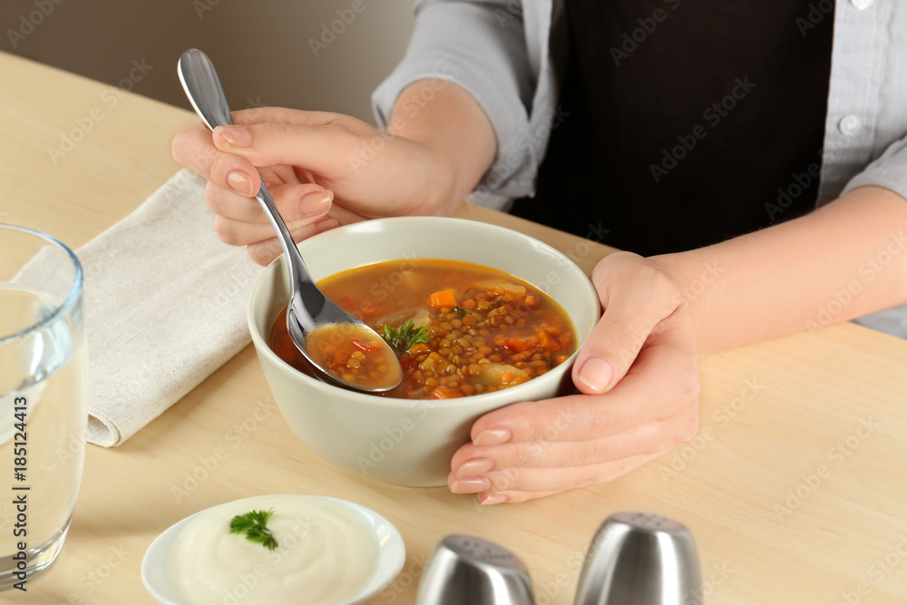 Woman eating tasty lentil soup at table