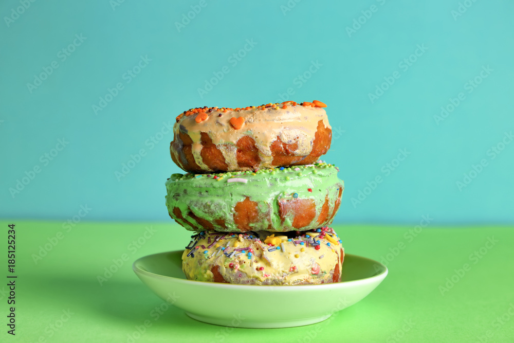 Plate with tasty donuts on color background