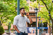 © Alexander Image - African American Man calling outside. Wearing gray shirt, rolling over sleeves, a black guy standing against light pole on street in New York, looking up, seriously listening to cell phone..