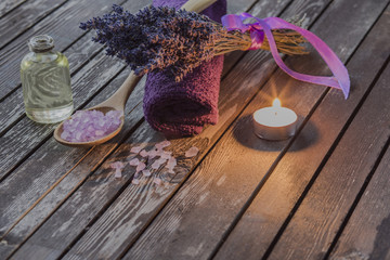 on a wooden table for spa items: oil, salt, towel, lavender, candles