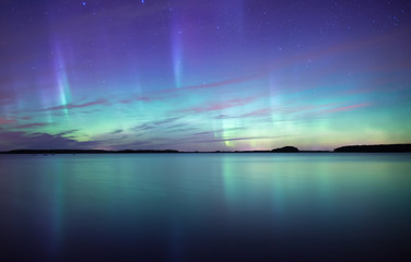 northern lights dancing over calm lake in farnebofjarden national park in sweden