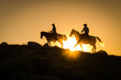 Silhouetted western cowboy and cowgirl on horseback against yellow sunset 