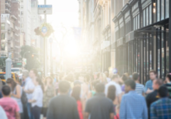 Wall Mural - Crowd of people walking down a busy street sidewalk in downtown Manhattan, New York City NYC with the bright glowing light of sunset in the blurred background