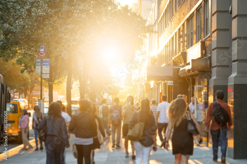 Fotomural Man stands in the middle of a busy sidewalk looking at his cell phone while crowds of people walk around on 14th Street in Manhattan, New York City with the glow of sunlight in the background