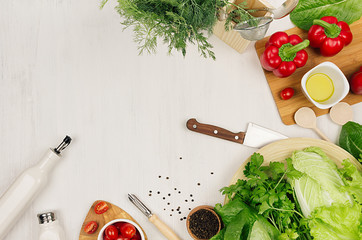 Wall Mural - Cooking fresh raw spring salad of green and red vegetables, spices, oil with wooden kitchenware on white wooden background, border, top view.