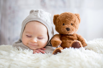 sweet baby boy in bear overall, sleeping in bed with teddy bear