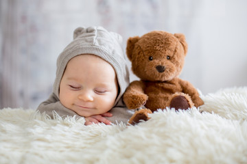 sweet baby boy in bear overall, sleeping in bed with teddy bear
