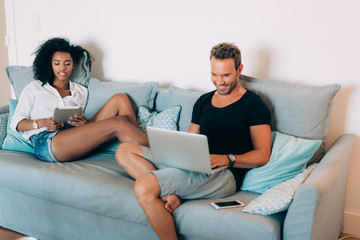 Wall Mural - Happy young couple relaxed at home in the couch on the mobile phone and computer