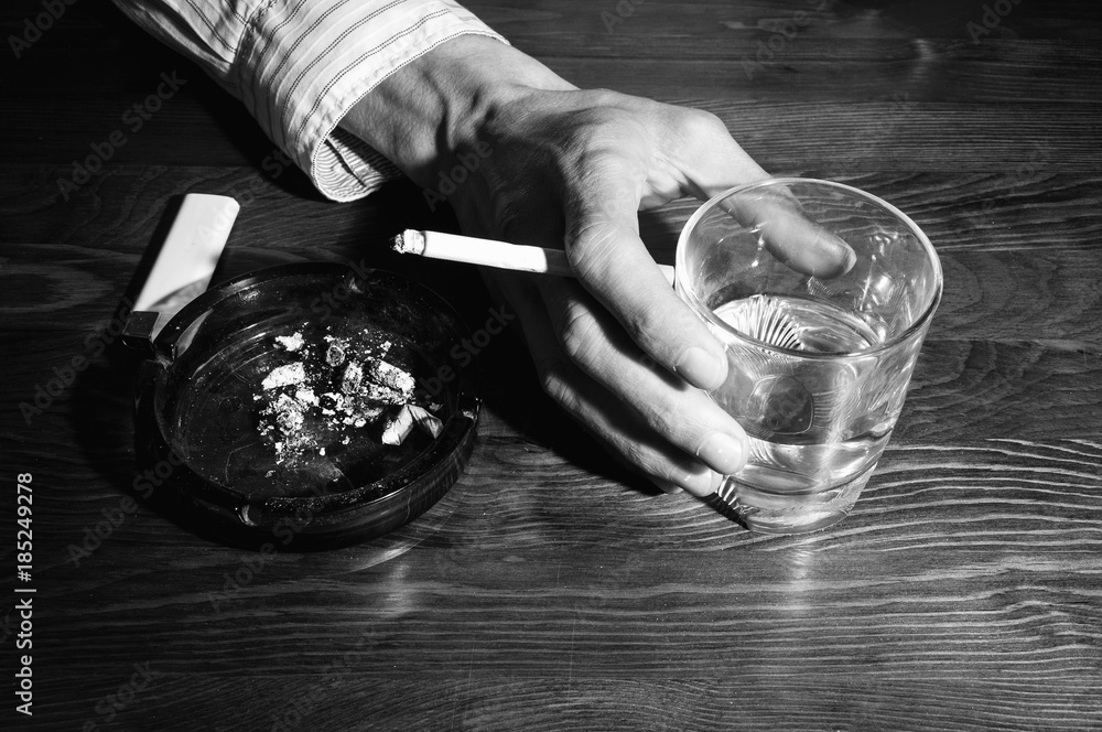 a glass and a cigarette Hands of alcoholic man holding a glass with alcohol drink with smoking  cigarette in the ashtray black and white Stock Photo