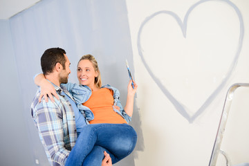 cheerful young love couple in new house painting decorating home and drawing a heart shape on the wall