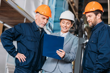 Wall Mural - male workers and female inspector in helmets in warehouse