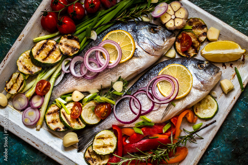 Plakat Dorada ryba z warzywami, cytryną, pikantność i zieleniami na błękitnym tle