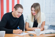 © okfoto - Pair of creative young people sit and work together sign document make plan. Man and woman discuss project write notes