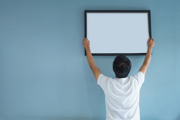 Asian man holding a picture frame on blue wall.