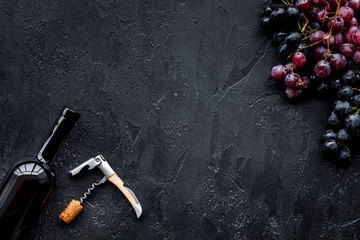 Uncorking the wine bottle. Bottle, corkscrew and bunches of red and black grapes on black background top view copyspace