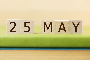 Wooden cube shape calendar for MAY 25 on green book, table. 