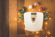 Top view of a white digital weight scale on wooden background surrounded with Christmas lights and decoration and snowy pine tree branches, weight gain during holidays concept, vintage toned