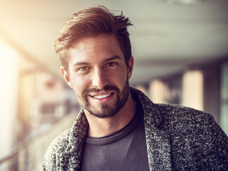 One handsome young man in urban setting in European city, standing, smiling and looking at camera