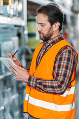 Wall Mural - male worker in safety vest writing in notepad in storehouse