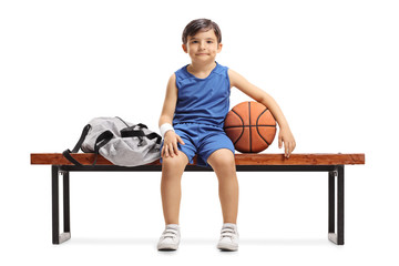 Canvas Print - Little basketball player sitting on a wooden bench next to a sports bag