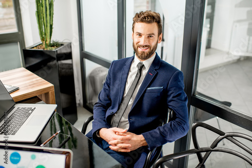 Portrait of a handsome banker working with laptop sitting at the luxury office i Poster Mural XXL