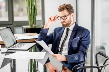 Portrait of a handsome banker working with laptop sitting at the luxury office interior with beautiful view on the skyscrapers