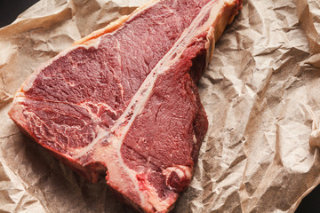 Wall Mural - Raw t-bone steak on craft papper on dark background