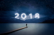 New year background, young man standing on a jetty in a lake and looking to the mountains under the dark sky with cloudy text 2018