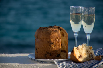 Sweet fruit Christmas and New Year cake panettone with two glasses with champagne served outside near blue sea