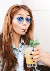 Poster - Funny crazy portrait of pretty hipster girl wearing trendy jeans clothes, drinking cocktail, surprised emotions.Cute young woman in summer outdoor cafe.