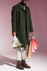 Stylish young african american man holding bouquet of flowers and bright shopping bags